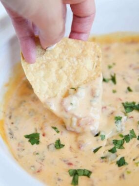 A tortilla chip dipped into creamy Rotel sausage dip garnished with chopped cilantro.