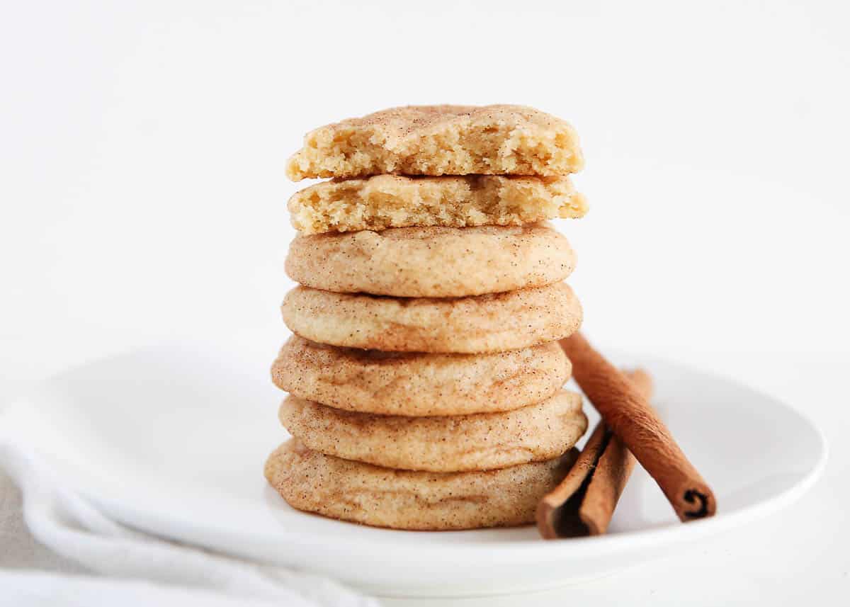 Stack of snickerdoodle cookies with cinnamon sticks on white plate.