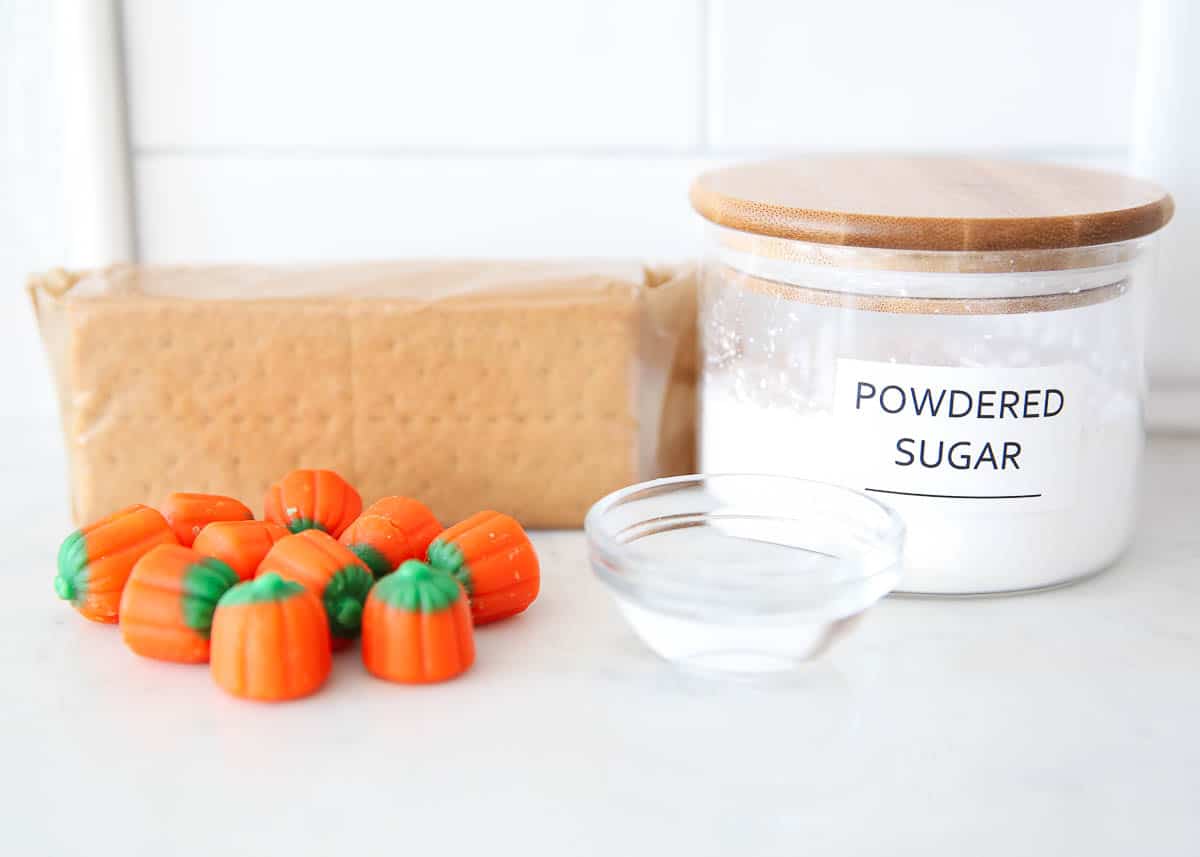 Halloween gingerbread house ingredients including graham crackers, pumpkin candies, powdered sugar and water.