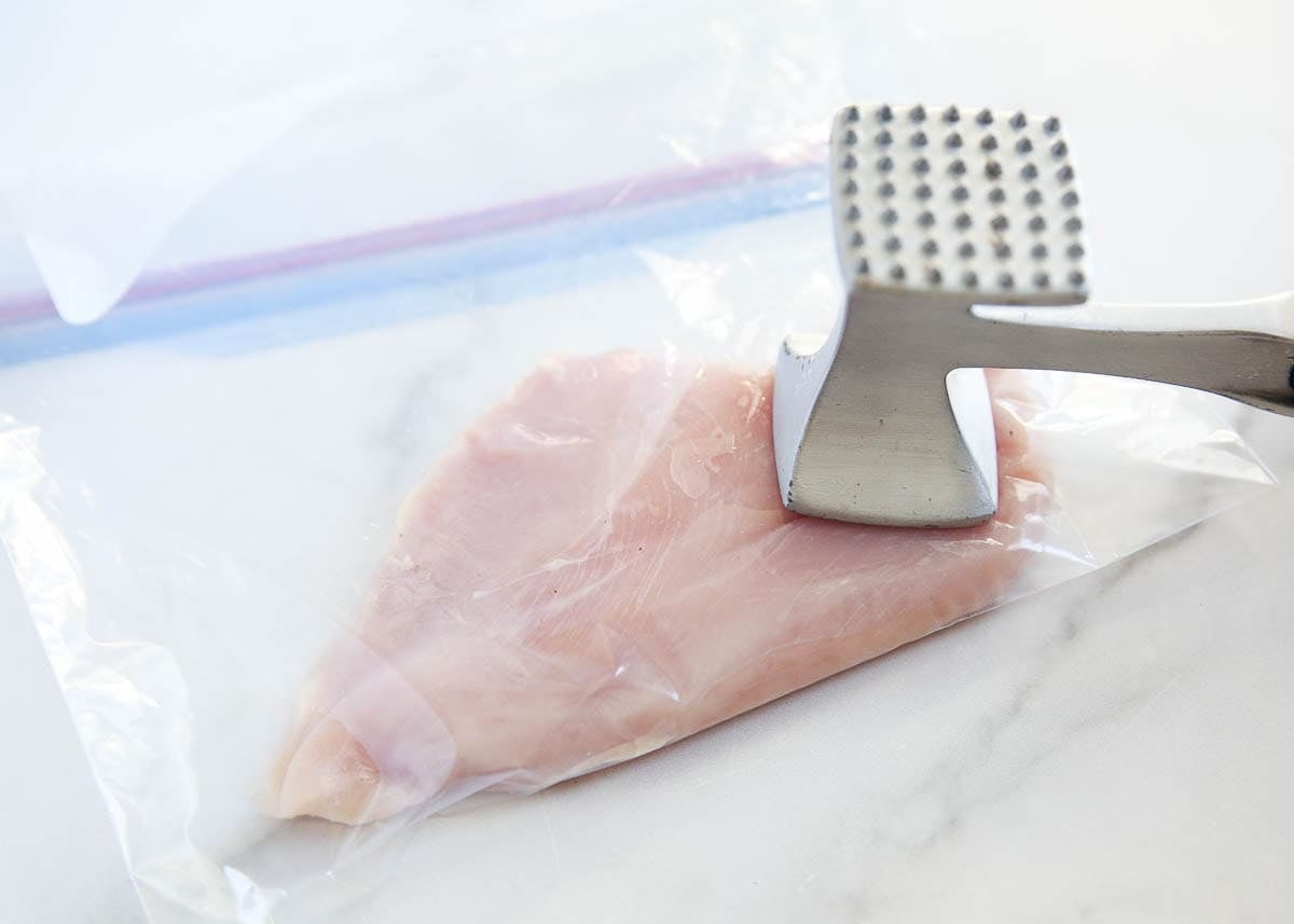 Pounding chicken breast to even thickness with a meat mallet in a zip top bag.