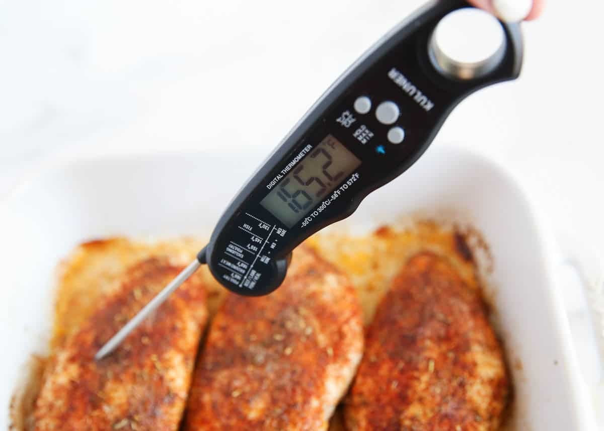 Checking internal temperature of baked chicken breast with a meat thermometer reading 165 degrees.