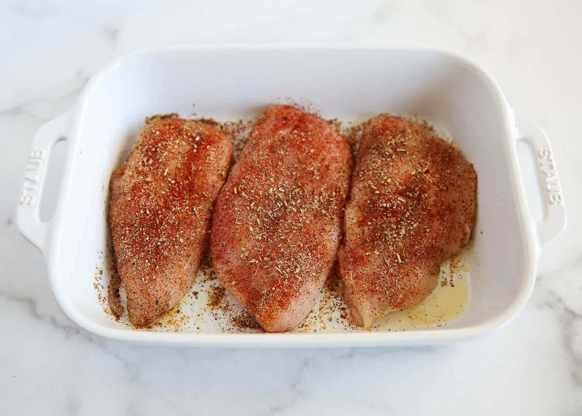 Seasoned chicken breasts in a white baking dish ready to go in the oven.