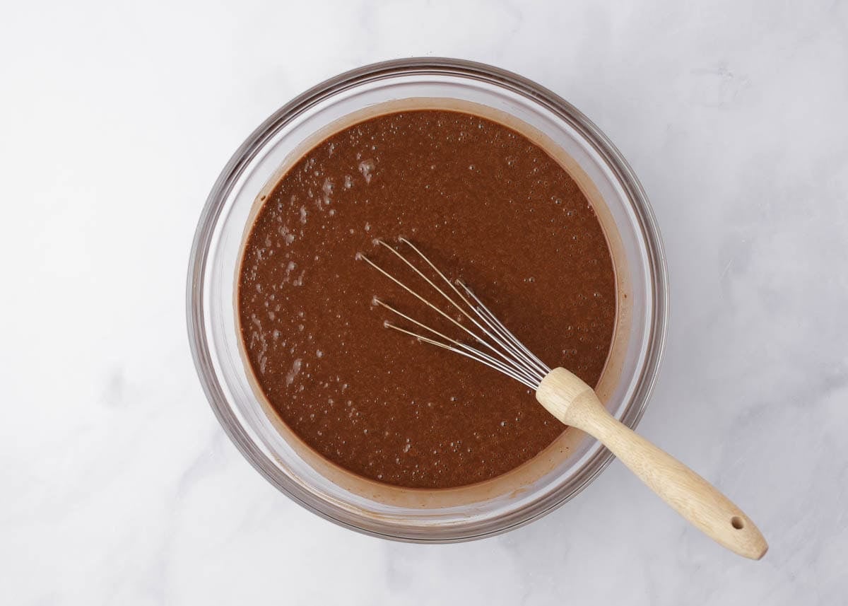 Chocolate cake batter whisked until smooth in a glass mixing bowl.