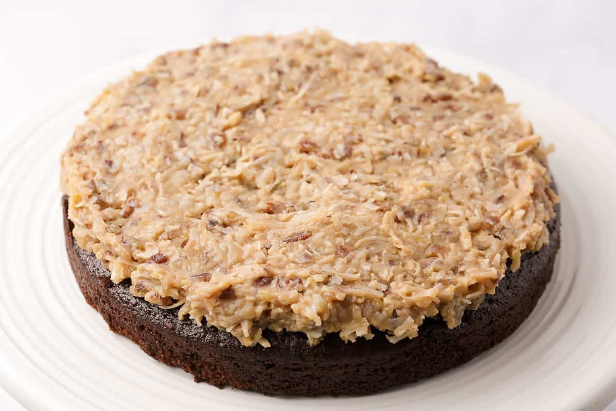 Coconut pecan frosting spread over a chocolate cake layer during assembly.