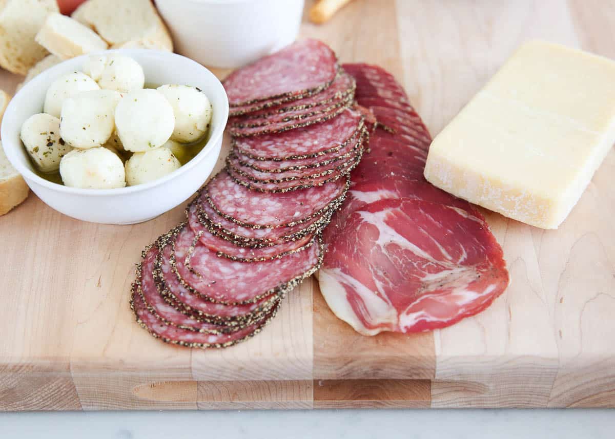 Wooden board with meats and cheese on top.