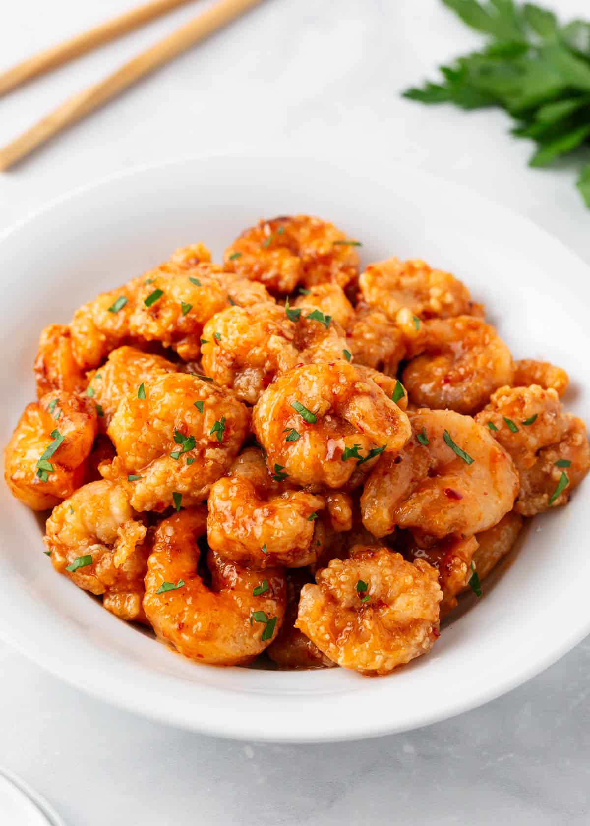 Crispy and delicious bang bang shrimp are inspired by the Bonefish Grill appetizer but easy to make at home! Shrimp are marinated in a flavorful buttermilk coating, fried, then drizzled with a sweet and spicy bang bang sauce. Crispy bang bang shrimp in a white bowl with parsley.