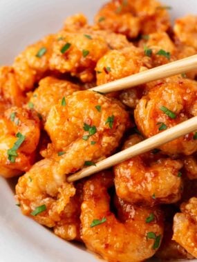 Crispy bang bang shrimp coated in creamy sauce served in a white bowl with chopsticks.