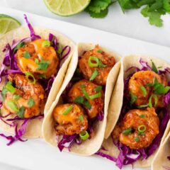 Four bang bang shrimp tacos tossed with cilantro and slaw on a white plate.