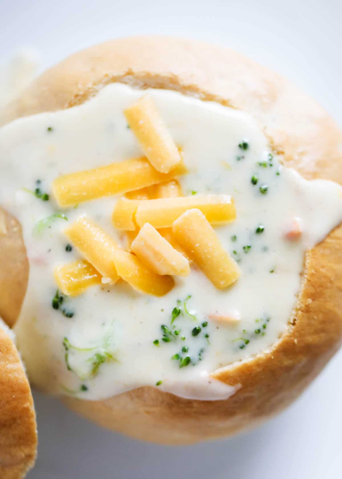A bread bowl with broccoli cheese soup in it with shredded cheddar garnished on top. 