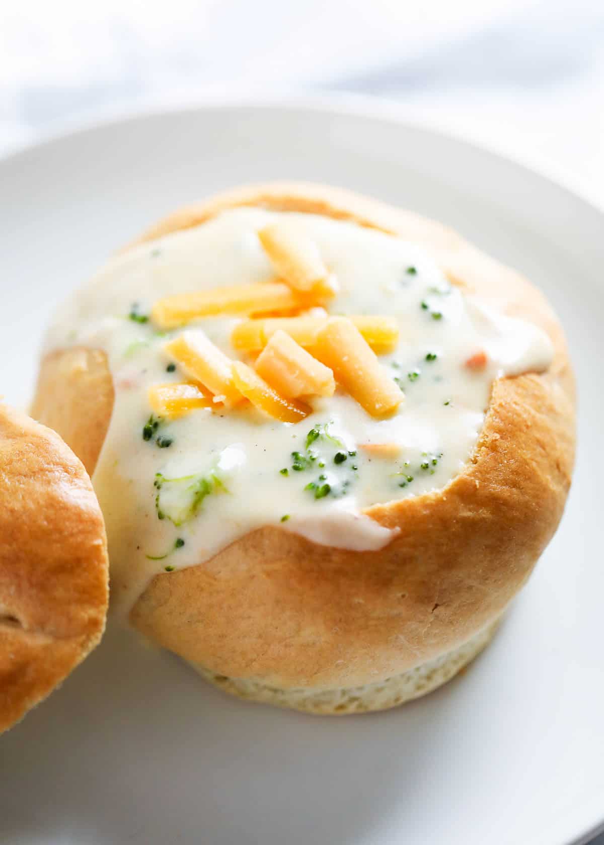 Broccoli cheese soup in a bread bowl on a white plate. 