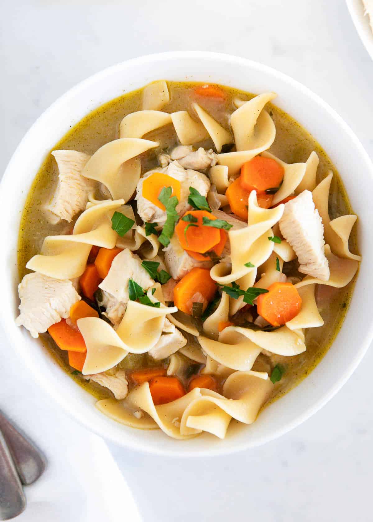 Noodle soup with chicken and vegetables in a white bowl.