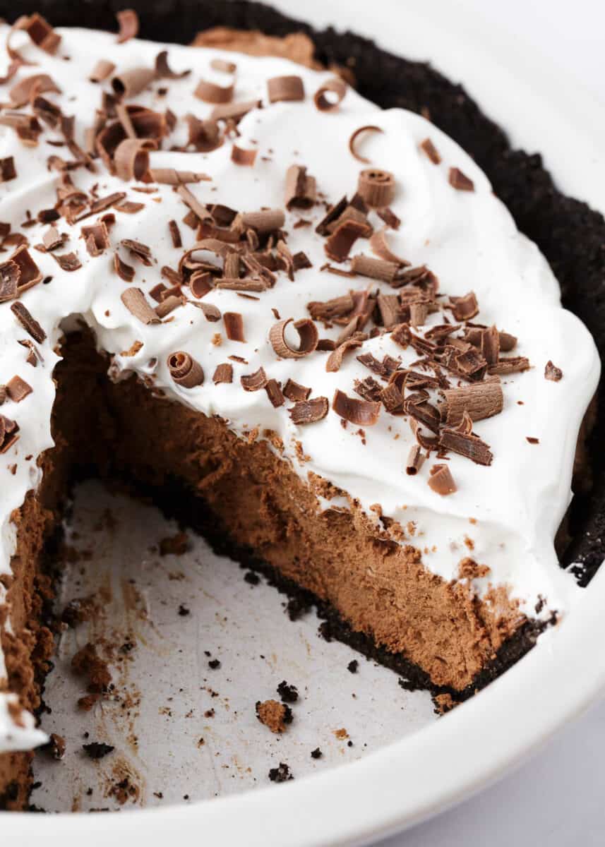 The ultimate chocolate silk pie made with a chocolate crust, silky smooth chocolate filling and topped with homemade whipped cream and chocolate shavings. This dessert is a chocolate lovers dream! Slice of chocolate silk pie in pie pan.