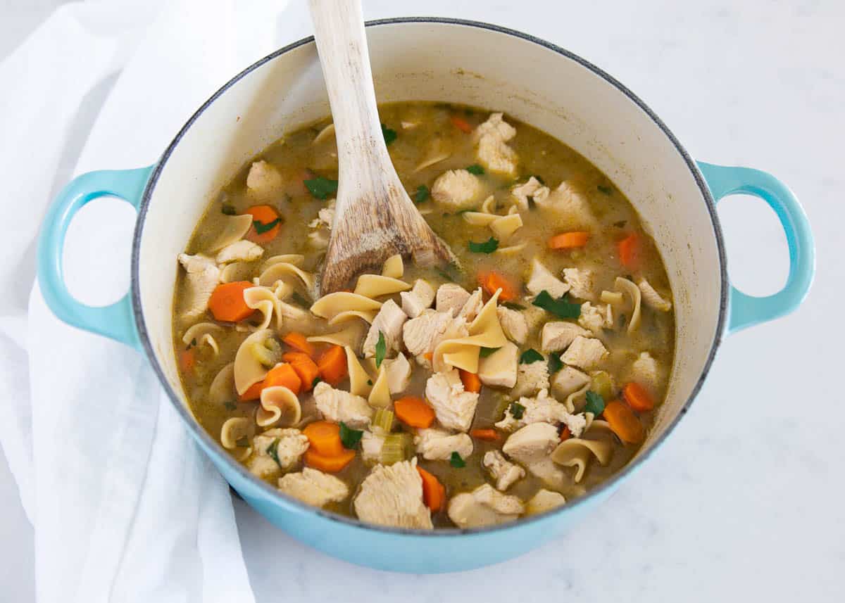 Chicken noodle soup cooked in a blue pot.