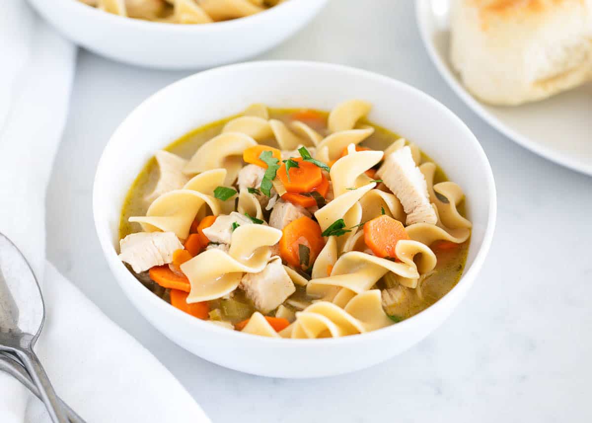 Chicken noodle soup in a white bowl with bread.