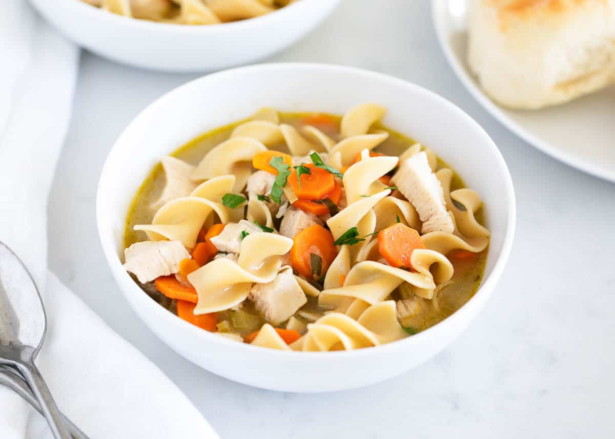 Chicken noodle soup is the perfect comfort soup on a chilly day. Simple to make and full of delicious flavor. It will become an instant favorite! Chicken noodle soup in a white bowl with bread.