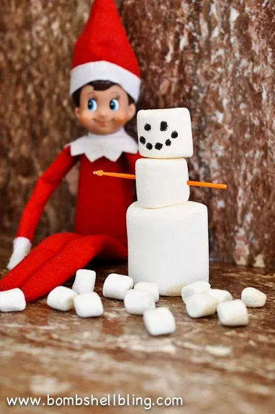 Elf sitting next to a marshmallow snowman. 