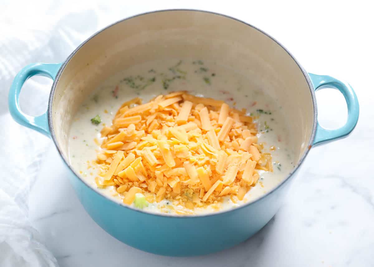 Broccoli cheddar soup in a stock pot pan with shredded cheddar ready to melt in the soup. 