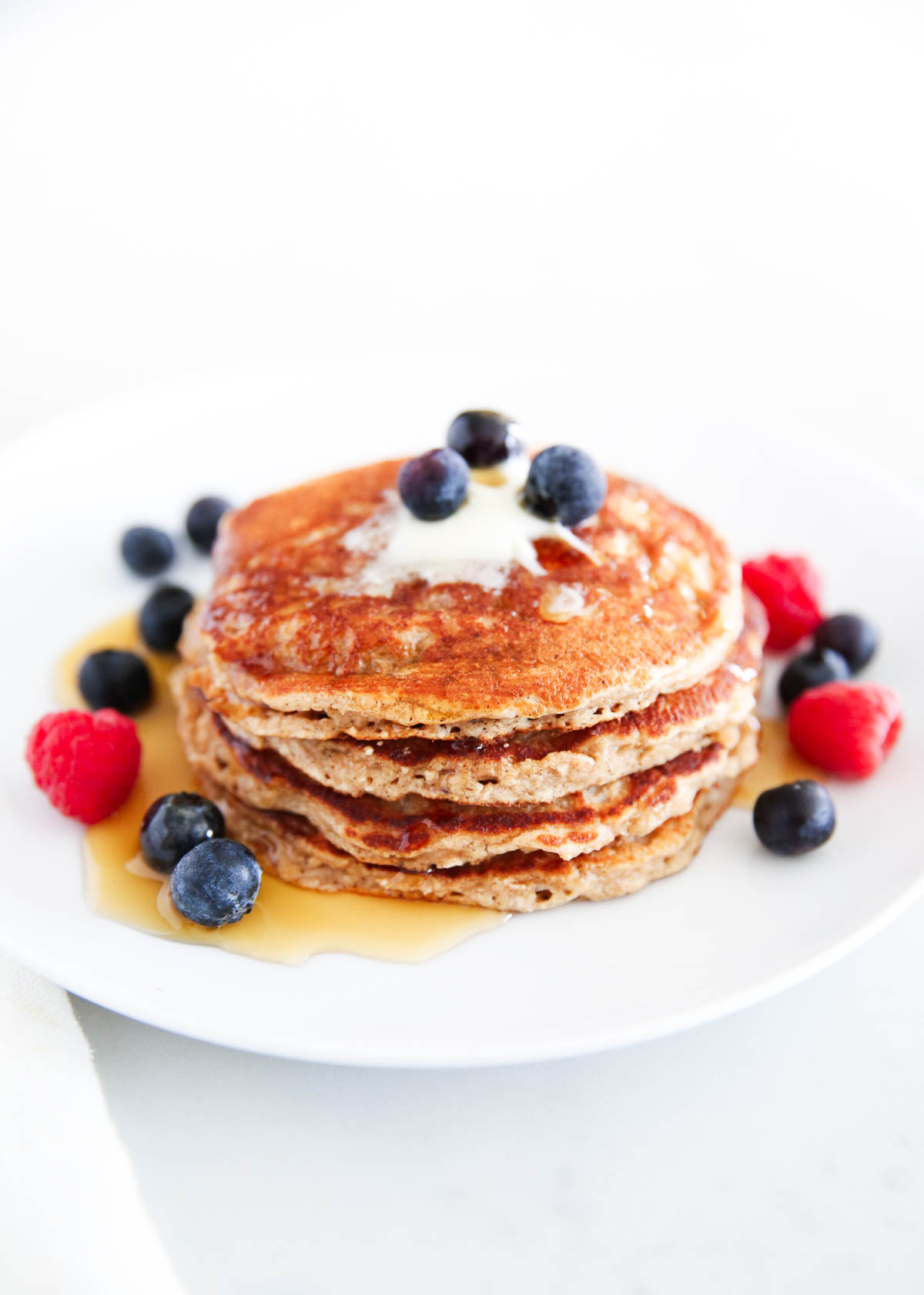 Stack of oatmeal pancakes on a white plate with berries.