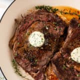 Cooking steak in the oven in a white skillet.