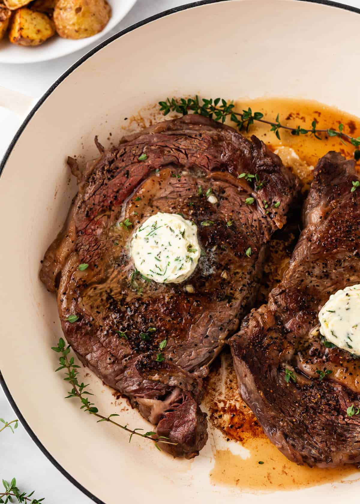 Cooking steak in the oven in a white skillet.