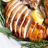 Sliced oven roasted turkey on a white plate with herbs.