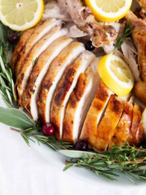 Sliced oven roasted turkey on a white plate with herbs.