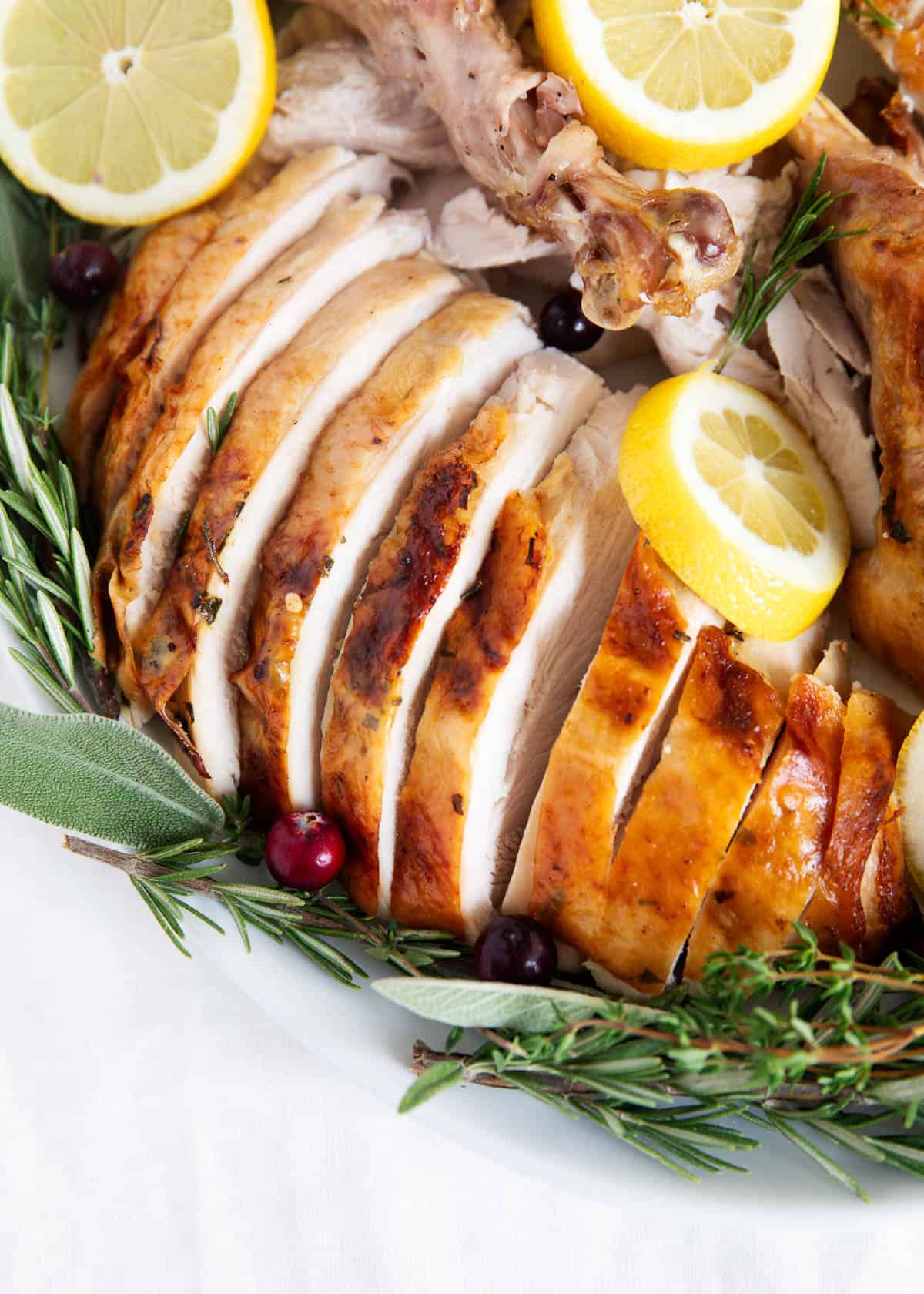Sliced oven roasted turkey on a white plate with herbs.