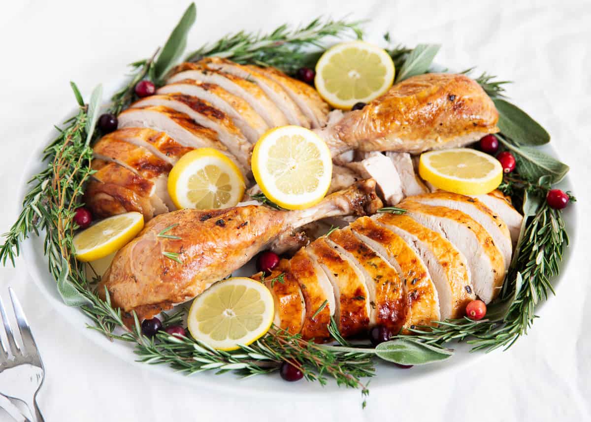 Juicy and tender oven roasted turkey stuffed with fresh herbs and coated in a flavorful garlic butter. This delicious dish will become the star of your holiday dinner table! Sliced oven roasted turkey on a white plate.
