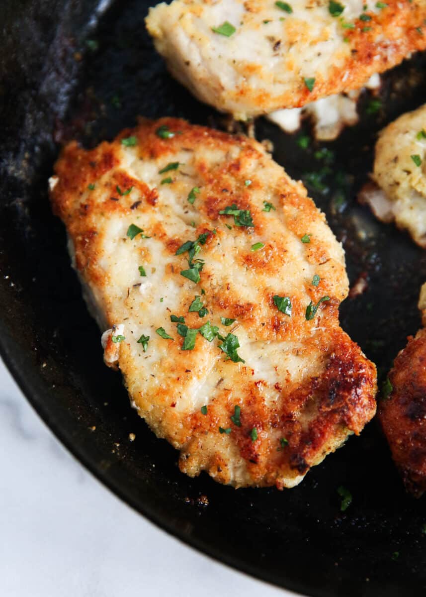 Parmesan crusted chicken cooked in a black skillet.