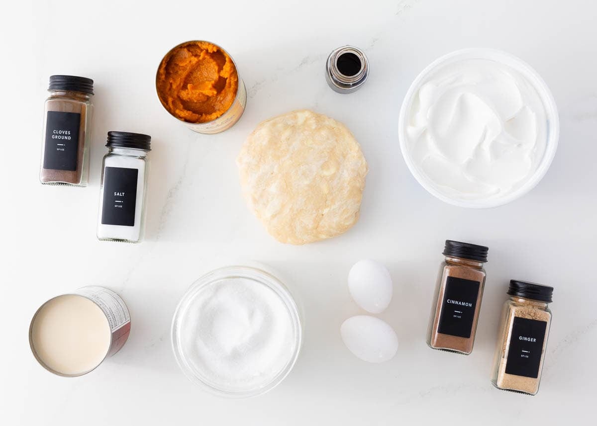 Ingredients for pumpkin pie including pumpkin puree, evaporated milk, sugar, vanilla, spices eggs and pie crust.