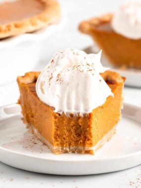 Easy homemade pumpkin pie sliced on a plate with whipped cream.