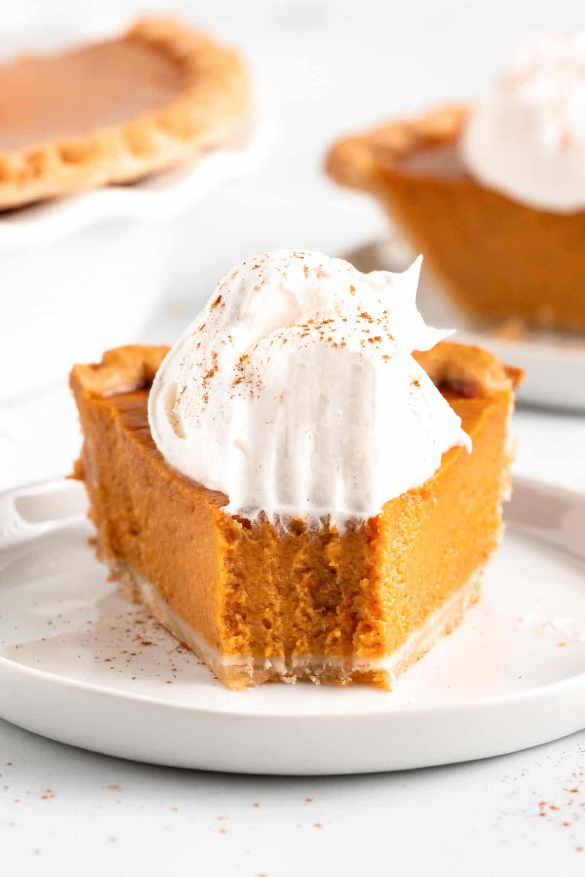 An up close photo of pumpkin pie with a dollop of whipped cream on top with a bite taken out of the front of the pie. 