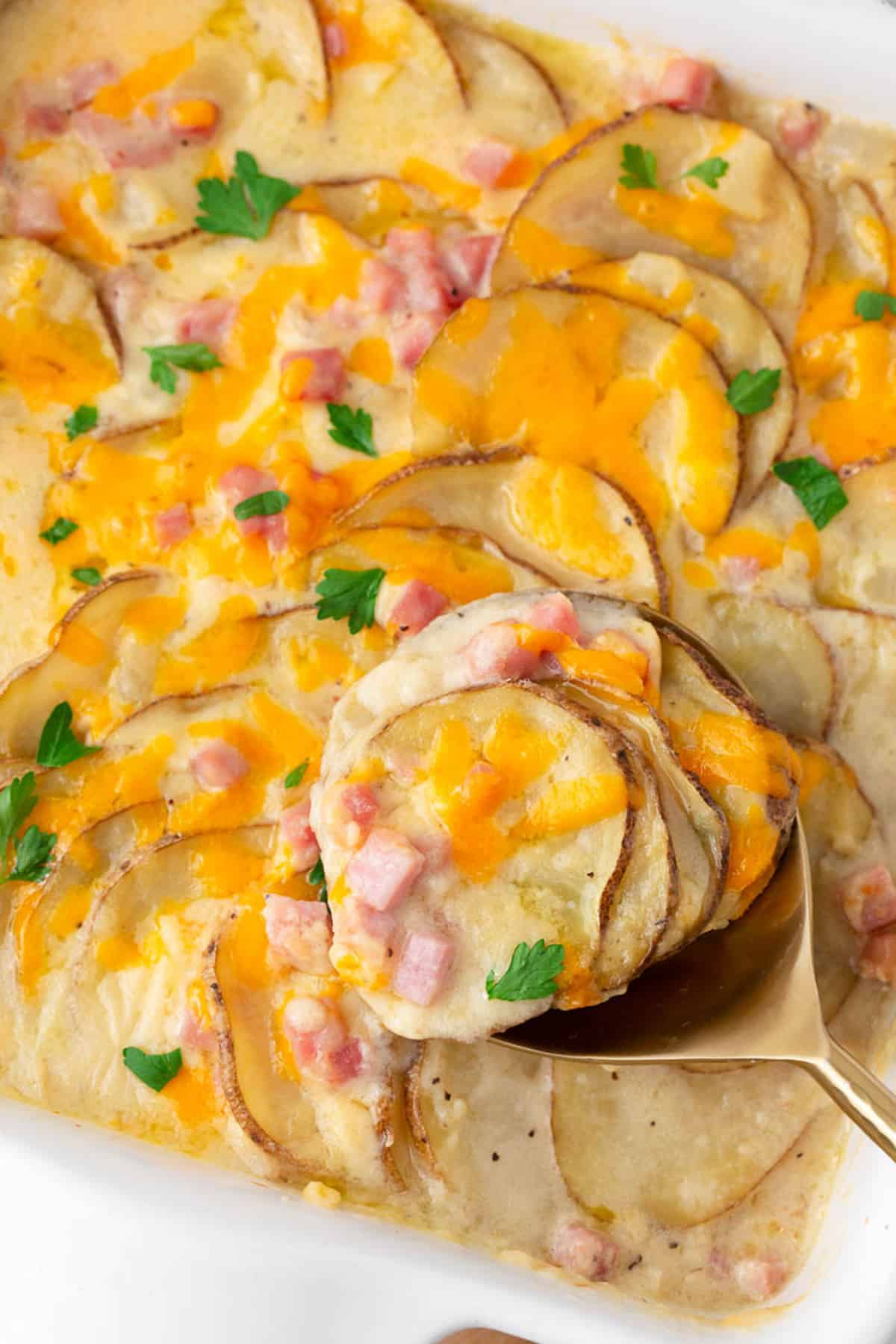 Simple, delicious and comforting, cheesy scalloped potatoes and ham is made with layers of tender sliced potatoes and leftover ham covered in a rich creamy sauce. It's the best casserole to serve as a dinner main or side dish! Scalloped potatoes and ham in a baking dish.