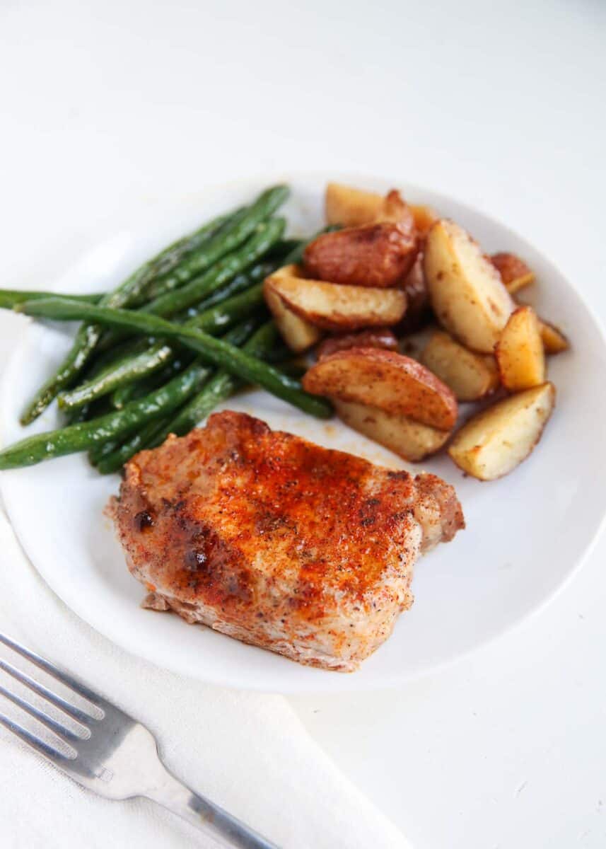 Pork chops with potatoes and green beans on a white plate.