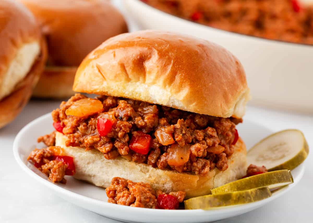 Turkey sloppy joes on a white plate with pickles.