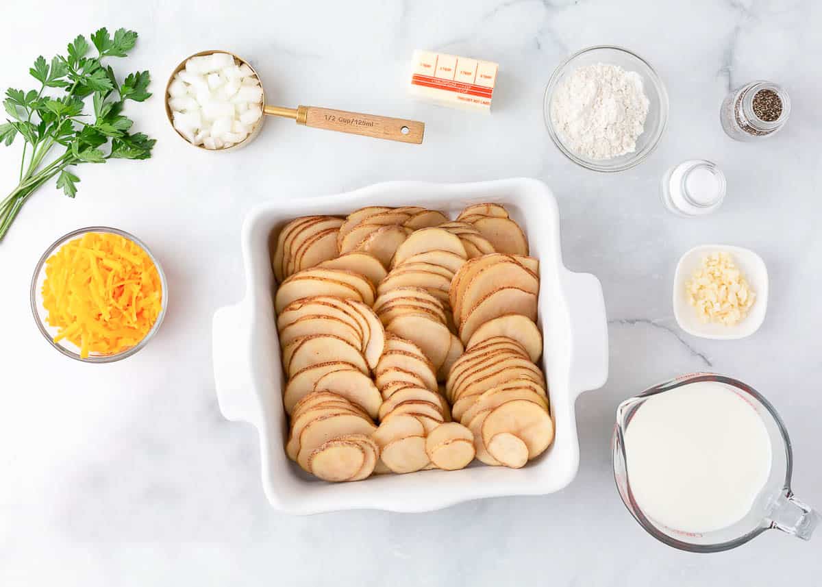 Scalloped potato ingredients on countertop, potatoes, cheese, milk, butter, flour and garlic.