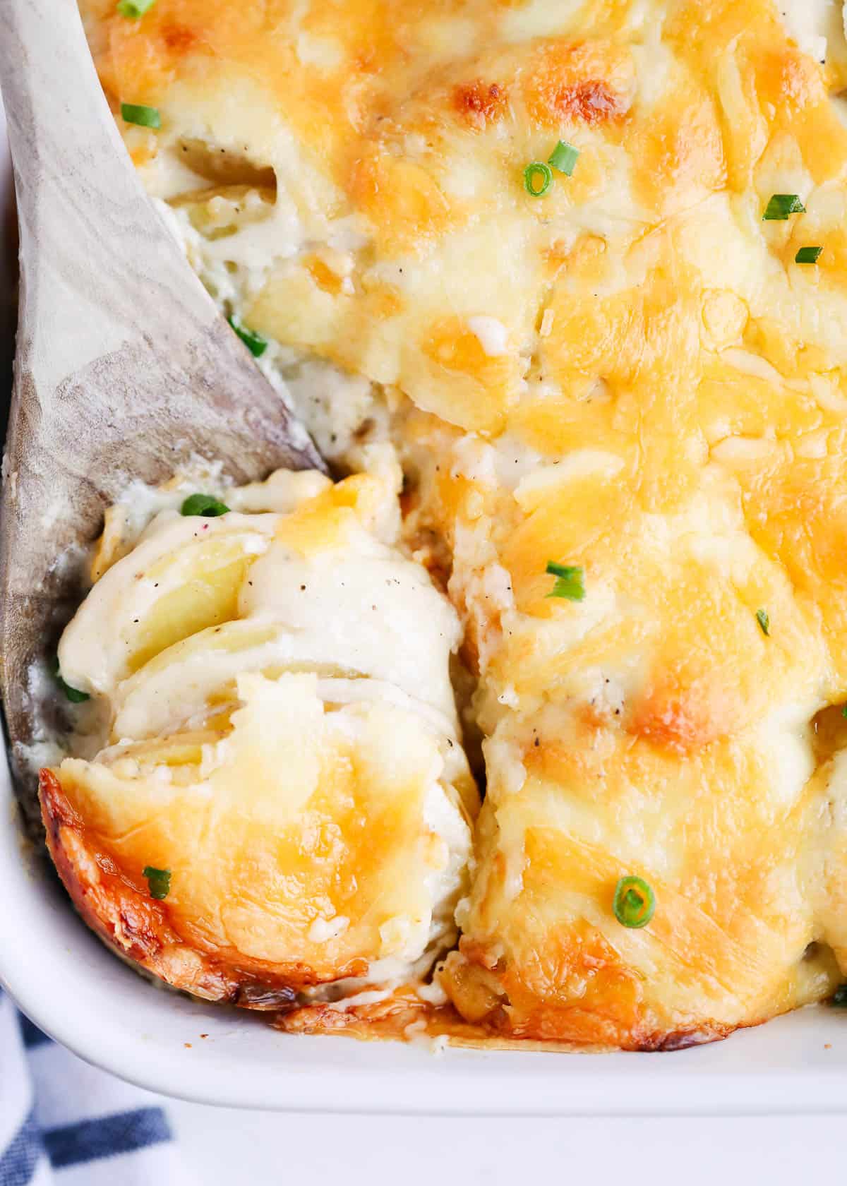 Cheesy scalloped potatoes in a baking dish with a wooden serving spoon.