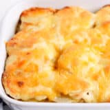 Cheesy scalloped potatoes in a white baking dish.