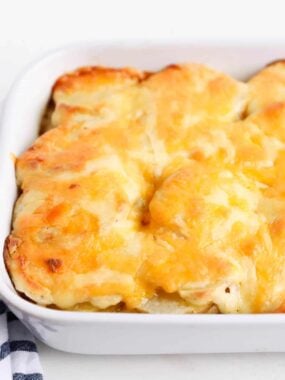 Cheesy scalloped potatoes in a white baking dish.