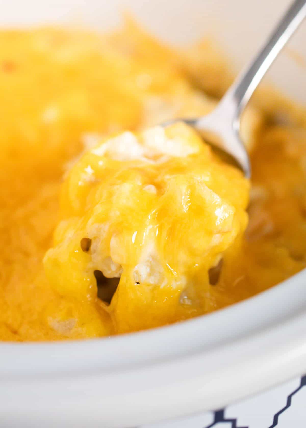 Cheesy potatoes on a silver spoon being lifted out of the crockpot. 