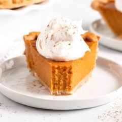 Close-up of a creamy pumpkin pie slice topped with whipped cream on a white plate.
