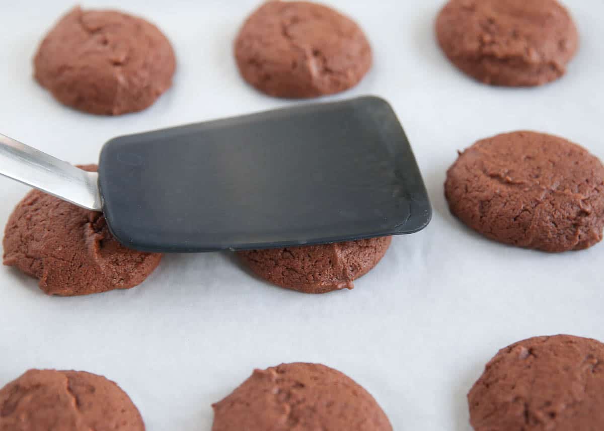 These Andes Mint cookies are made with an Andes mint melted on top of a soft-baked chocolate cookie! Sprinkle more mint chocolate chunks on top for an indulgent treat. Flattening cookie dough balls with a spatula.