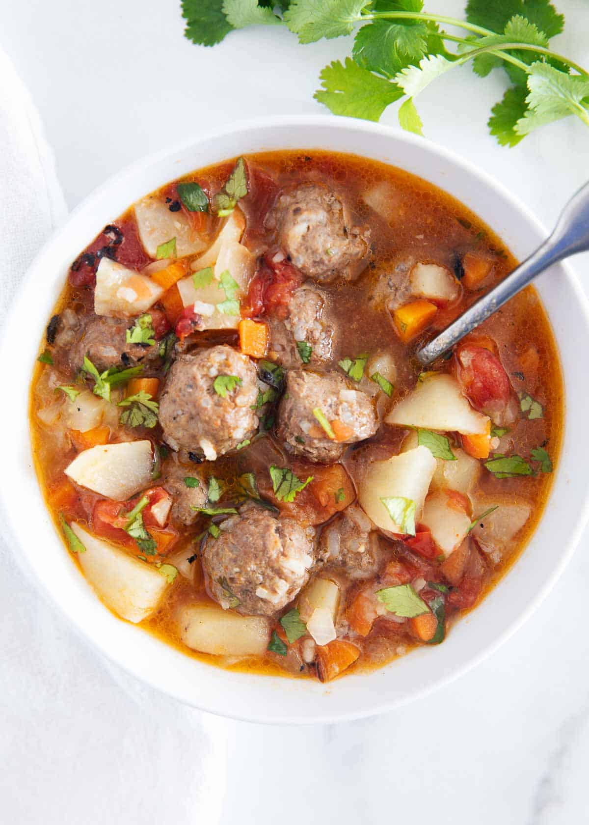 Albondigas soup is made with beef and rice meatballs, potatoes, vegetables, tomatoes and onions. It's super flavorful, hearty and the perfect dish to warm you up on a chilly day. Albondigas soup in a white bowl.
