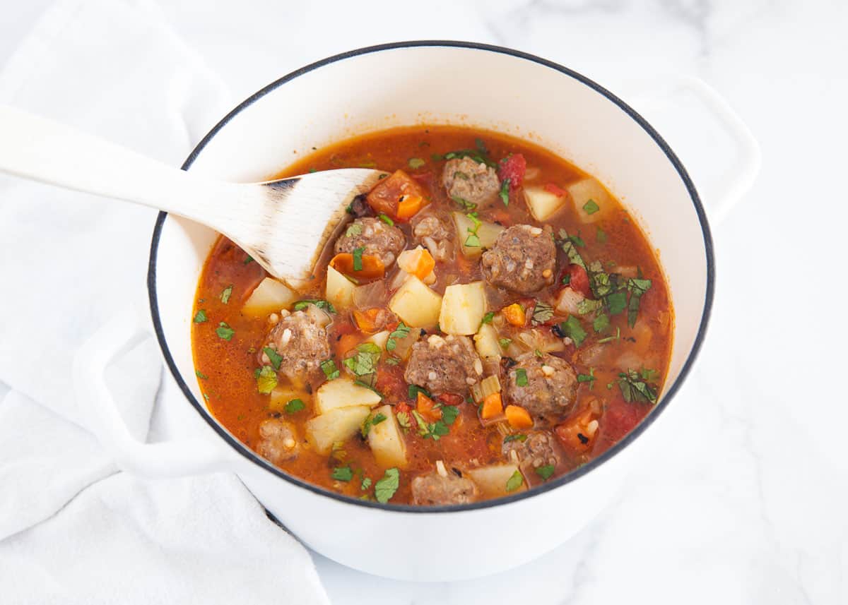 Albondigas soup in a white pot with a wooden spoon.