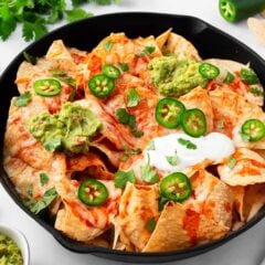 Baked nachos with cheese and toppings in a cast iron skillet.