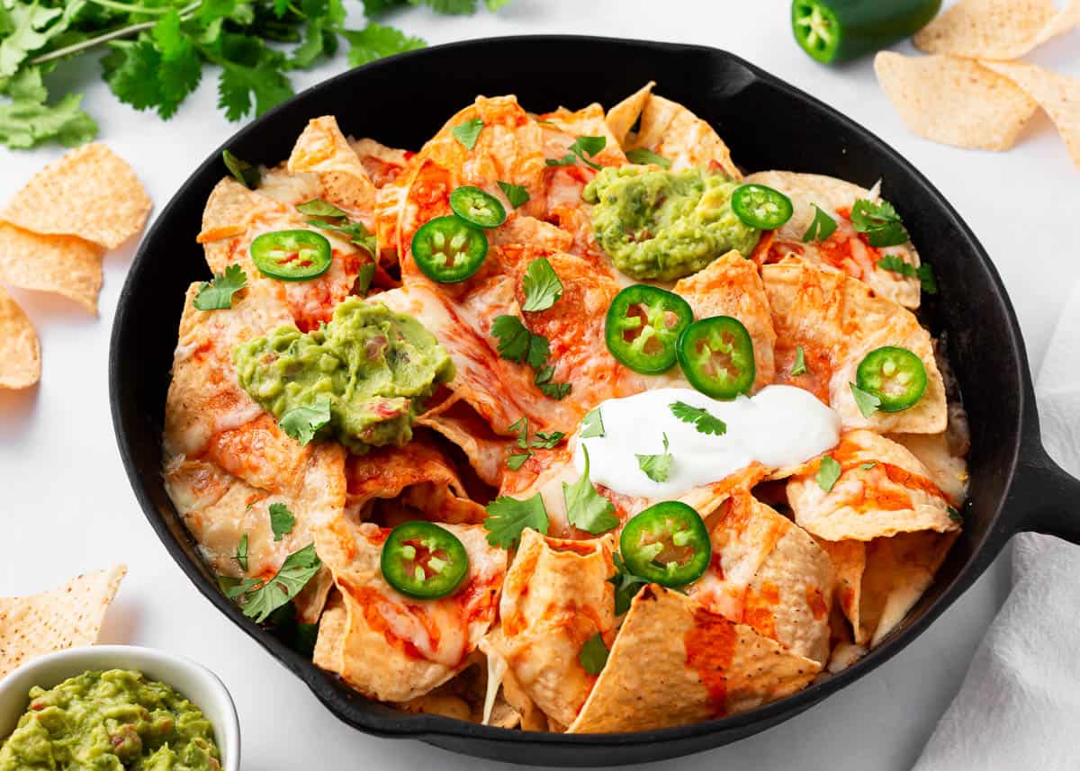 Baked nachos with toppings in a cast iron skillet.