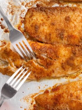 Baked tilapia on a baking pan with two forks showing flaky texture.