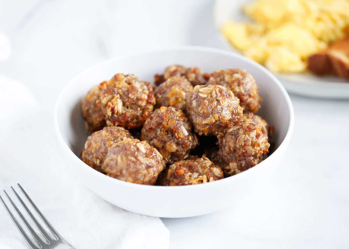 These delicious breakfast meatballs can be rolled the night before and then baked in the oven in the morning. Loaded with sausage, cheese, apples, and maple syrup, this easy breakfast dish sets you up for the day ahead! Breakfast meatballs in a white bowl.
