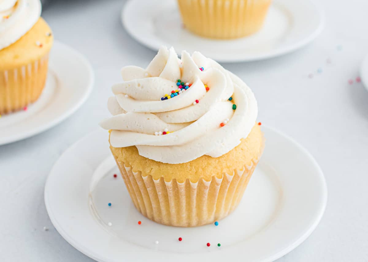 This light and fluffy buttercream frosting will become one of your staple recipes when baking! It's made with only 4 ingredients and is perfect on cupcakes, cookies, cakes and more. Buttercream frosting topped on a vanilla cupcake.