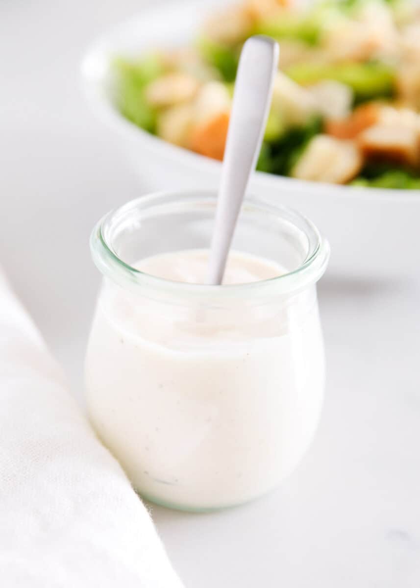 Caesar salad dressing in a glass jar with a spoon. 